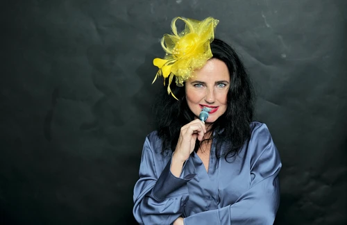 schwarzhaarige Frau in blauer Bluse mit gelbem Hütchen am Kopf