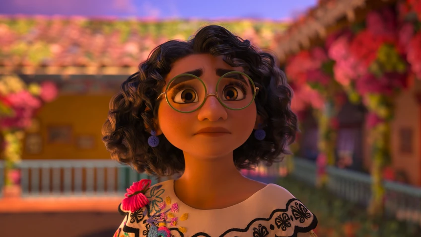 Ein dunkel gelocktes Mädchen mit Brille vor einem Haus, das mit Blumen geschmückt ist