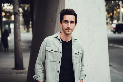 Mann in hellem Hemd und dunklen Haaren vor einem Betonpfeiler