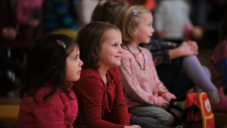 Publikumsfoto vom "Tonspiele"-Projekt "Schnee" - einem Projekt des Musikvermittlungsprogramm des Tonkünstler-Orchester Niederösterreich. Zu sehen sind fröhliche Kinder, die gespannt zuhören und -schauen.