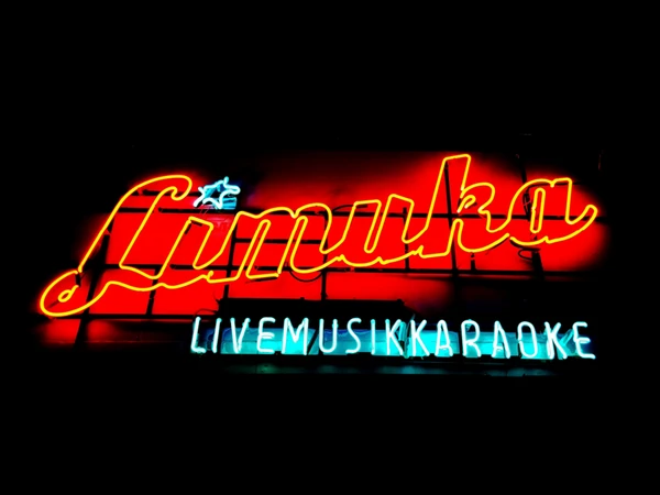 Logo von "LiMuKa" - dem Projekt "Live-Musik-Karaoke" bei dem alle die wollen auf der Bühne - begleitet von einer Liveband - Songs covern können. Das Logo ist der "Limuka"-Schriftzug in roter Leuchtschrift sowie der Zusatz "Live Musik Karaoke" in hellblauer Schrift.