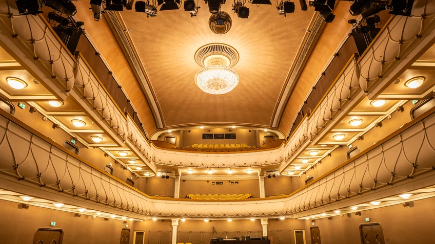 Theatersaal mit bernsteinfarbener Bestuhlung, Kristallluster, der Lichter an die Decke wirft