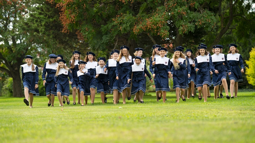 eine Gruppe Mädchen in Uniform mit Hüten läuft über eine Wiese auf die Kamera zu