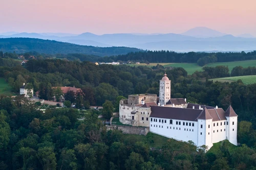 Luftaufnahme der Schallaburg inmitten grüner Hügel bei Sonnenuntergang.