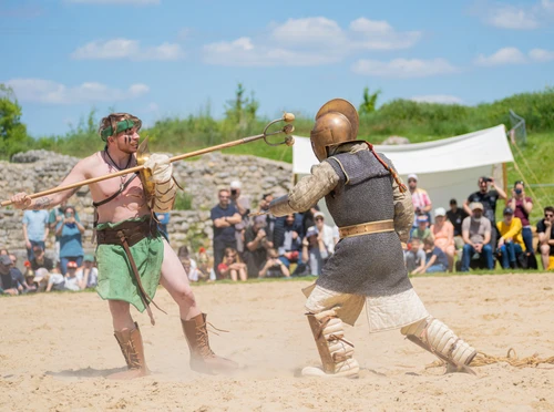 Two gladiators are fighting a exhibition match in the ruins of an ancient amphitheater before a crowd of amazed spectators