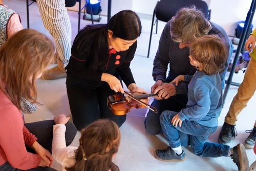 Eine Musikerin erklärt Kindern und Eltern, wie man über eine Geige streicht