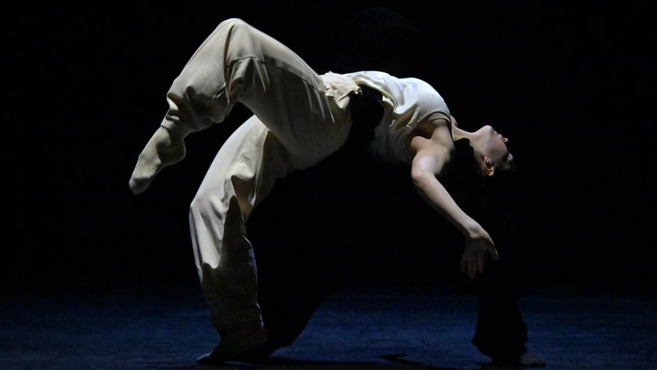 Performancefoto der Choreografie "Frontier" von Crystal Pite. Zu sehen ist ein:e Tänzer:in des Ballet BC weißgekleidet in einer dynamischen Tanzbewegung vor schwarzem Bühnenhintergrund.