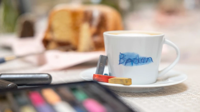 Kaffee, Kuchen und kreative Materialien wie Buntstifte und Kreide auf einem Museumstisch während des Programms KUNST MELANGE im Museum