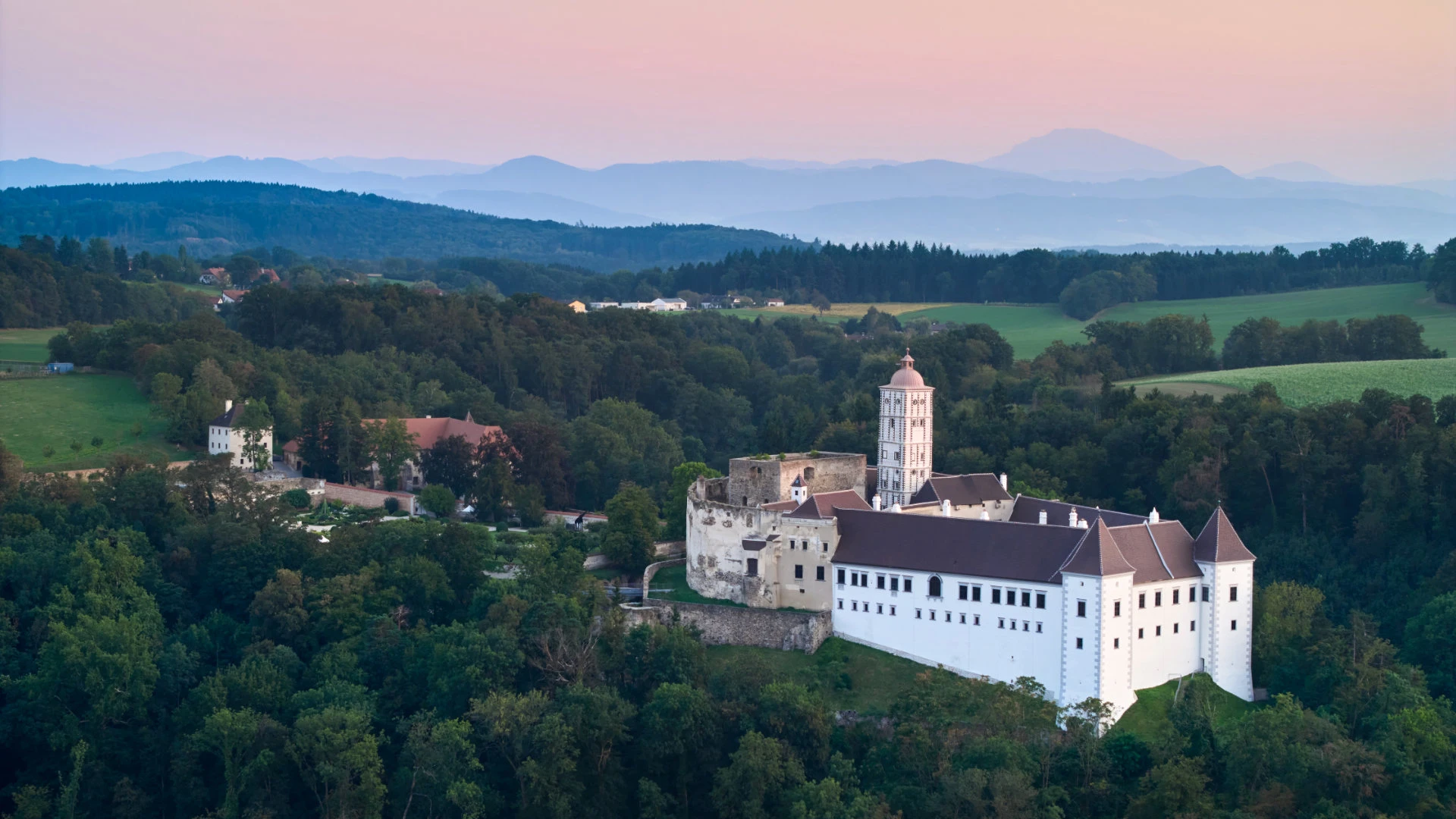 Luftaufnahme der Schallaburg inmitten grüner Hügel bei Sonnenuntergang.