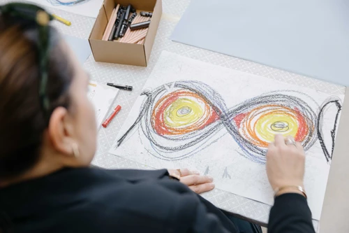 Hände die mit bunten Stiften auf weißes Papier zeichnen