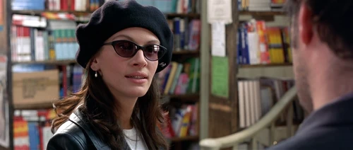 Frau mit schwarzem Hut und Sonnenbrille, dahinter Bücherregale