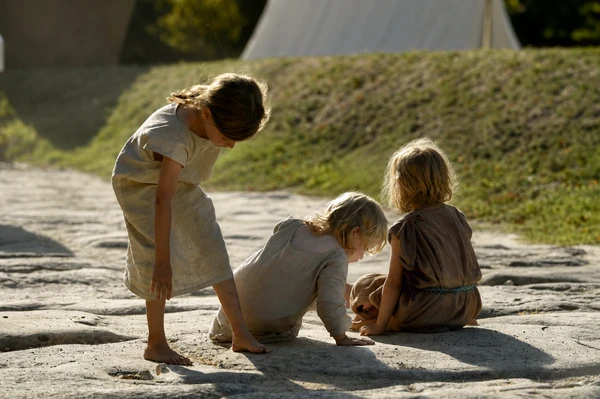 Three children in tunics are playing in the street at the Late Antiquity Festival 2017; the sun is shining