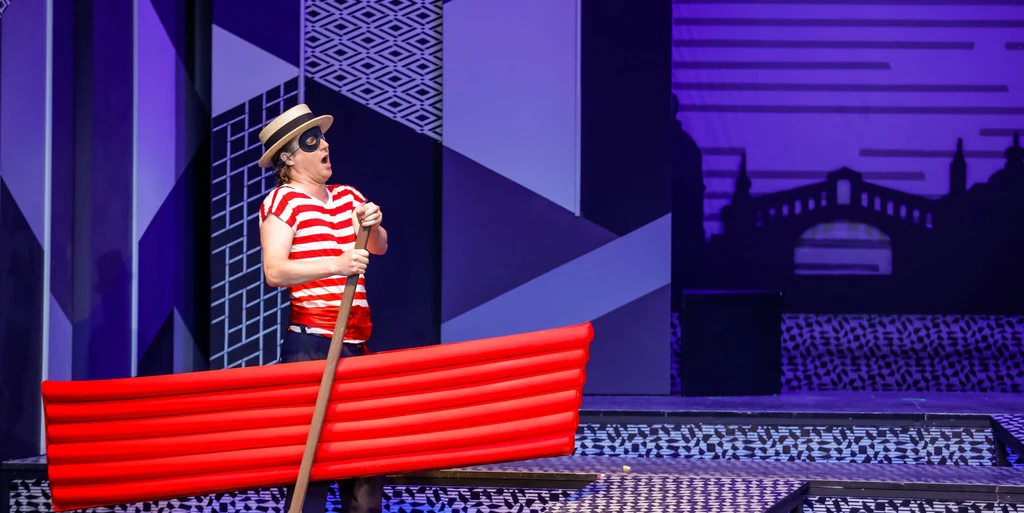 singender Mann mit Maske und mit roter Luftmatratze, im Hintergrund abstrakte blaue Muster 