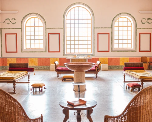 Interior view of the thermal hall with Roman klines surrounding a stone water basin. There are murals on the ceiling and walls.