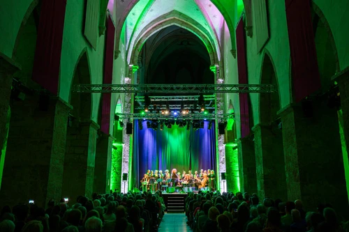 Konzert in gotischer Hallenkirche mit grüner Beleuchtung Chor und Orchester auf der Bühne Publikum füllt den Saal