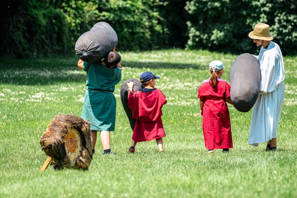 Children throwing stones at the 2023 Children's Festival; a man hands a stone to one of the children to throw 