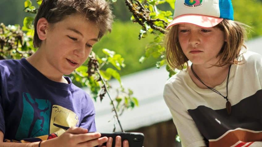 Zwei Kinder in der Natur schauen auf ein Handy