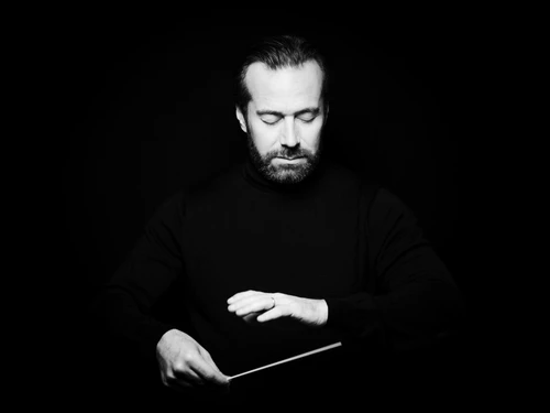 Ein Mann mit Dirigierstock vor schwarzem Hintergrund, er hat die Augen geschlossen