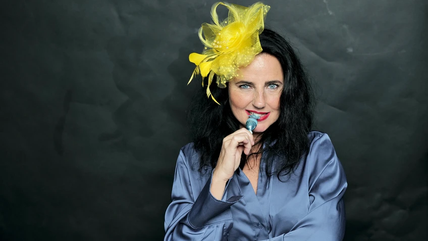 schwarzhaarige Frau in blauer Bluse mit gelbem Hütchen am Kopf