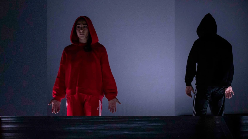 A performance photo from ‘Little Red Riding Hood’, choreographed by Sylvain Huc. The photo shows two dancers, one wearing a bright red tracksuit and the other a black tracksuit.