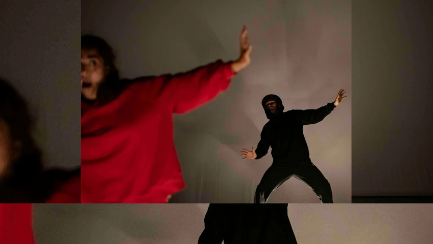 Performancefoto von "Rotkäppchen", choreografiert von Sylvain Huc. Zu sehen sind zwei Tänzer:innen, eine:r davon in einem knallroten Sportanzug, der:die andere in einem schwarzen Sportanzug.