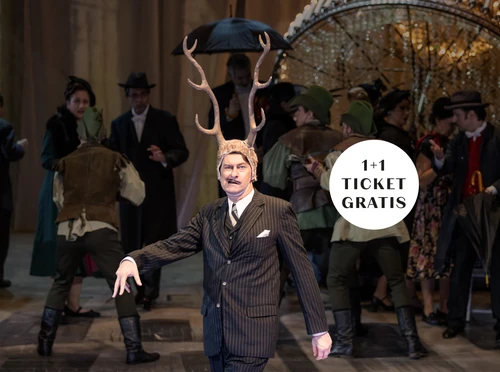 Ein Mann mit Schnurrbart in Nadelstreifanzug zeiht eine Grimasse, auf seinem Kopf trägt er ein Hirschgeweih, im Hintergrund Szenen einer Party, einige Personen sind als Jäger verkleidet, ein Kronleuchter liegt auf dem Boden. Störer mit 1+1 Ticket gratis im Bild.
