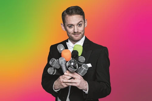 Mann mit vielen Mikrofonen in der Hand. Hintergrund ist grün, gelb, orange, rosa. Nahaufnahme.