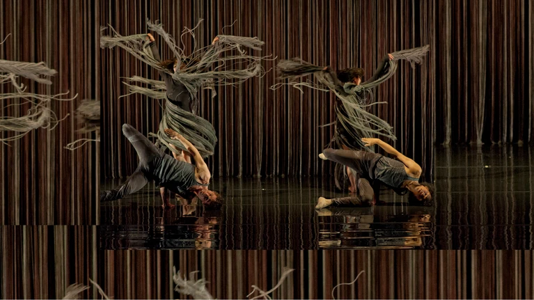 Performancefoto aus dem Tanzstück "Kaléidoscope", choreografiert von Mourad Merzouki, getanzt von der Compagnie Käfig. Zwei Tänzer:innen in wallenden dunkelgrünen Kleidern mit langen schwingenden Fransen drehen Pirouetten, während vor ihnen zwei Tänzer:innen, ebenfalls in grau/dunkelgrün gekleidet, synchron eine akrobatische Bodenfigur tanzen.