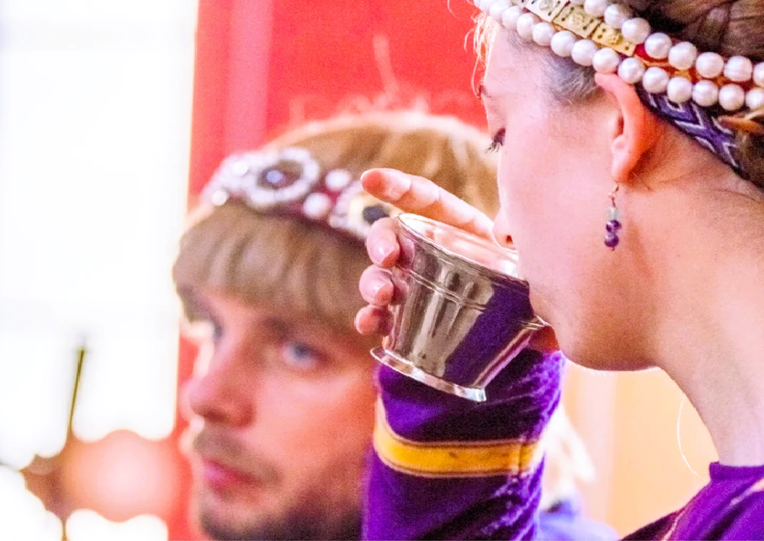 The empress drinks from a cup; the emperor lies in the background; both are dressed in purple during the Carnuntum time travel experience