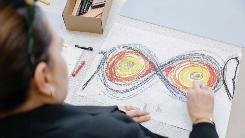 Hände die mit bunten Stiften auf weißes Papier zeichnen
