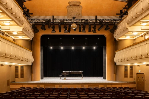 Innenansicht vom Stadttheater Wiener Neustadt mit leuchtend beleuchteter Bühne, schwarzem Vorhang und Konzertflügel.