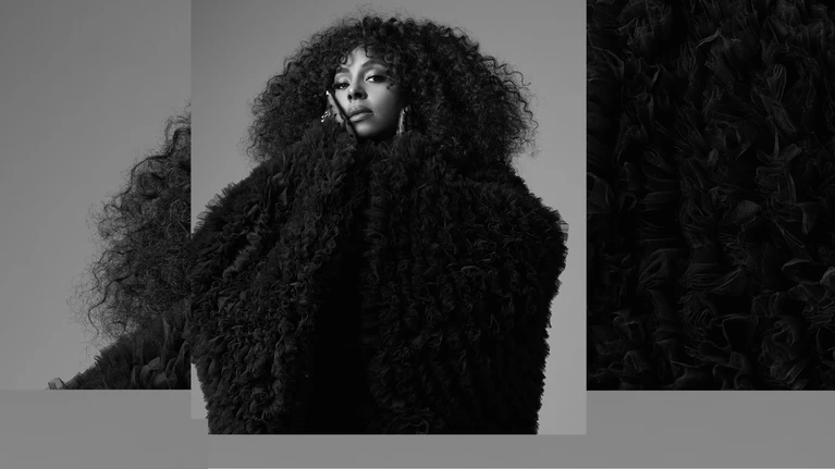 A black-and-white portrait of the musician Ledisi wearing a large black coat.