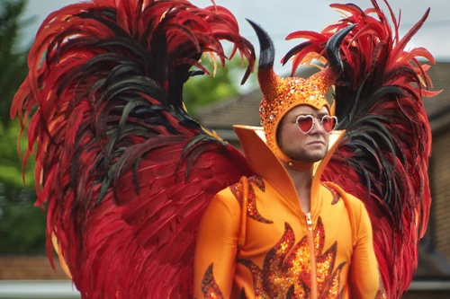 Mann mit Herzchen-Sonnenbrille in rot-orangem Federkostüm mit Hörnern