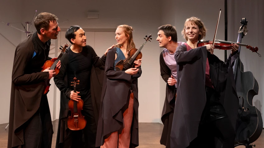 Fotoimpression aus dem Probenprozess zu "Fledermäuse" von der schallundrauch agency. Die Künstler:innen tragen schwarze Capes und halten ihre Streichinstrumente in Händen.