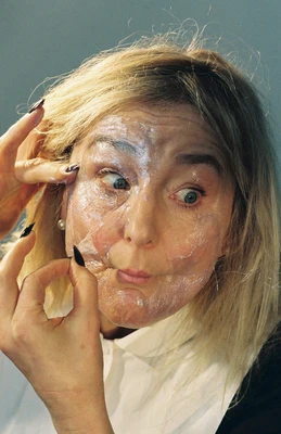 Nahaufnahme einer Frau, die sich eine Art Gesichtsmaske vom Gesicht zieht und die Augen weit aufreißt