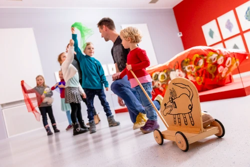 Kinder und Erwachsene bewegen sich gemeinsam durch einen Museumsraum mit spielerischen und kreativen Objekten.