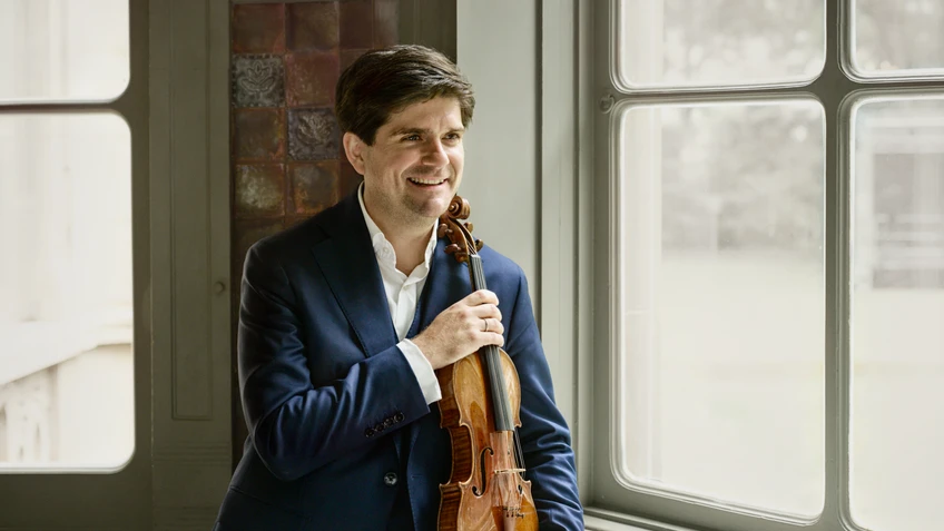 Photograph of smiling violinist Fedor Rudin, seen with his instrument. 