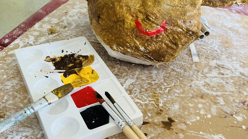 Pappeskulptur mit langen Ohren und angemalt. Vorne sind Pinsel und Farben zu sehen.