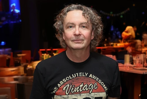 Mann mit grauen, halblangen Haaren vor unscharfem Hintergrund