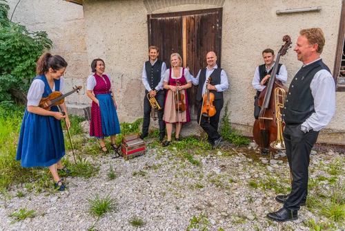 Musikgruppe in Tracht mit Instrumenten im Schotter vor einem alten Gebäude