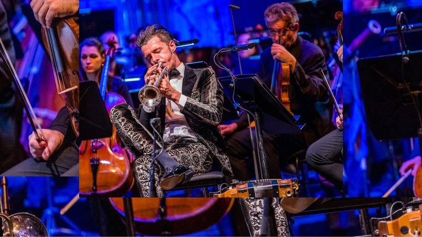 Konzertfoto von Herbert Pixner mit eine Trompete spielend, hinter ihm zu sehen: das Tonkünstler Orchester Niederösterreich auf einer blau beleuchteten Bühne.