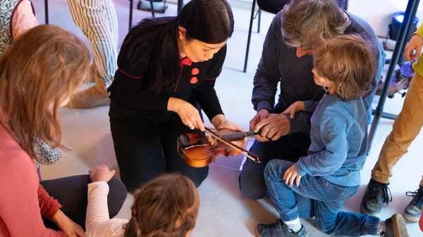 Eine Musikerin erklärt Kindern und Eltern, wie man über eine Geige streicht
