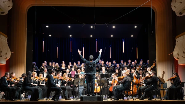 Orchester, Dirigent und Sänger musizieren auf einer Bühne