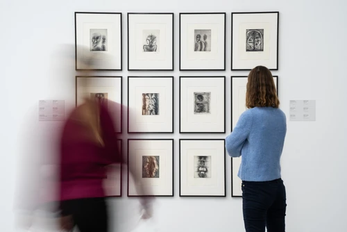 Zwei Frauen betrachten kleinteilige Bilder an einer Galeriewand.