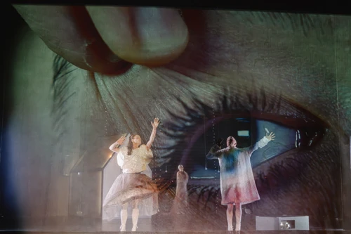 Menschen auf einer dunklen Bühne, dahinter Projektionen