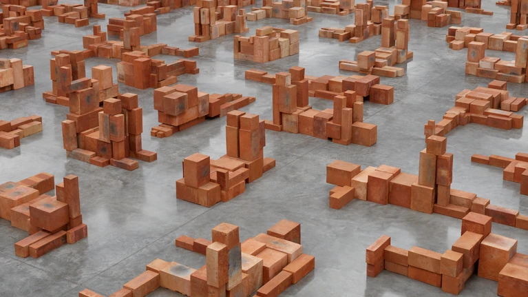 Foto von Antoney Gormleys Installation „Resting Place II“ (2024), bestehend aus gestapelten Terrakotta-Steinblöcken in einem hellgrauen Galerie-/Museumsraum.