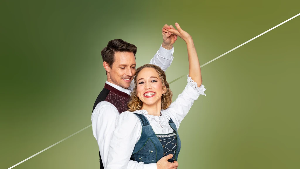 Grüner Hintergrund, davor Mann und Frau in Tanzpose, beide tragen Tracht. Der Mann blickt Frau lächelnd an, Frau lacht in die Kamera.