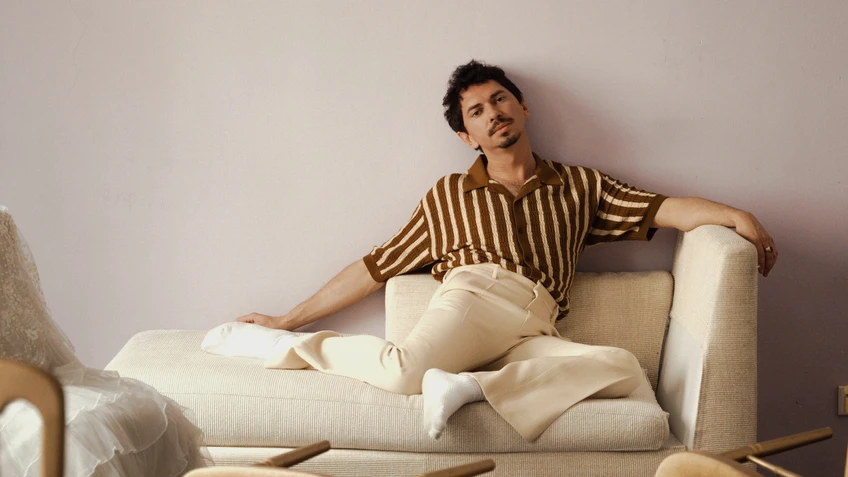 Julian Le Play sitzend auf einem hellen Sofa vor einer blassrosa Wand. 