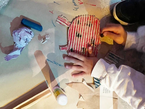 Children's hands making and painting a ladybird out of cardboard.