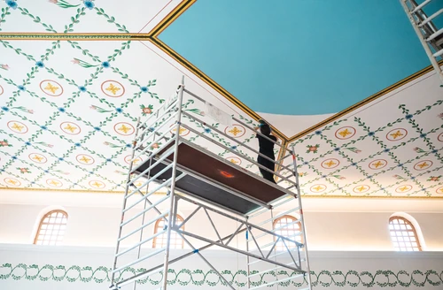 Reconstruction work on the ceiling of the sala thermarum; the decorated ceiling is visible, with a female painter standing on scaffolding 